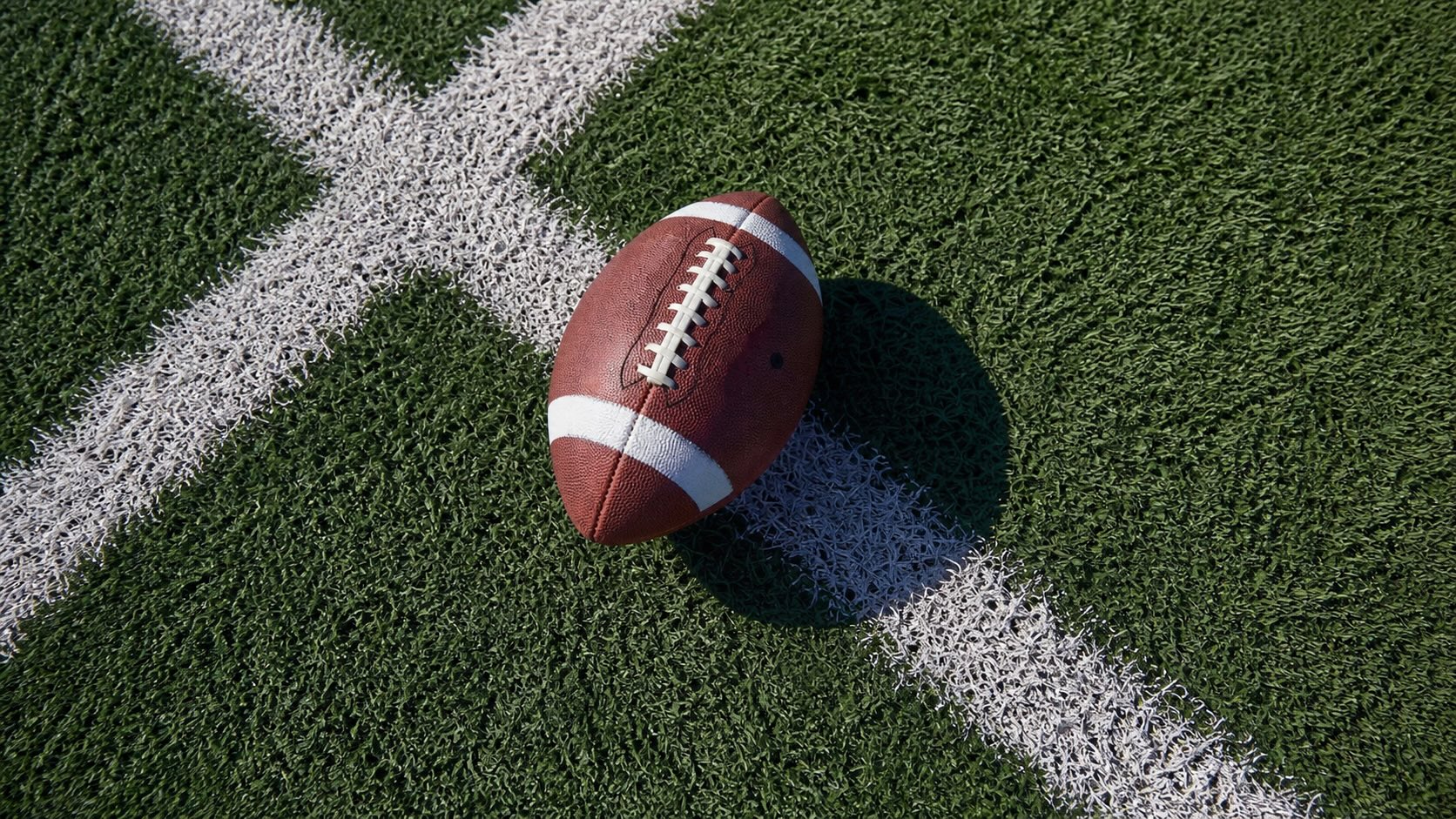 Football resting on green turf beside white yard lines on a football field.